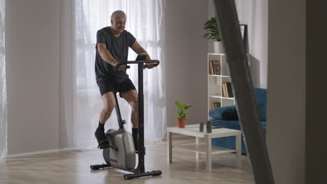 Gesunder-Lebensstil-Und-Fitness-Im-Mittleren-Alter-Person-Ist-Training-Mit-Stationären-Fahrrad-In-Home-Cardio-Training-Drinnen